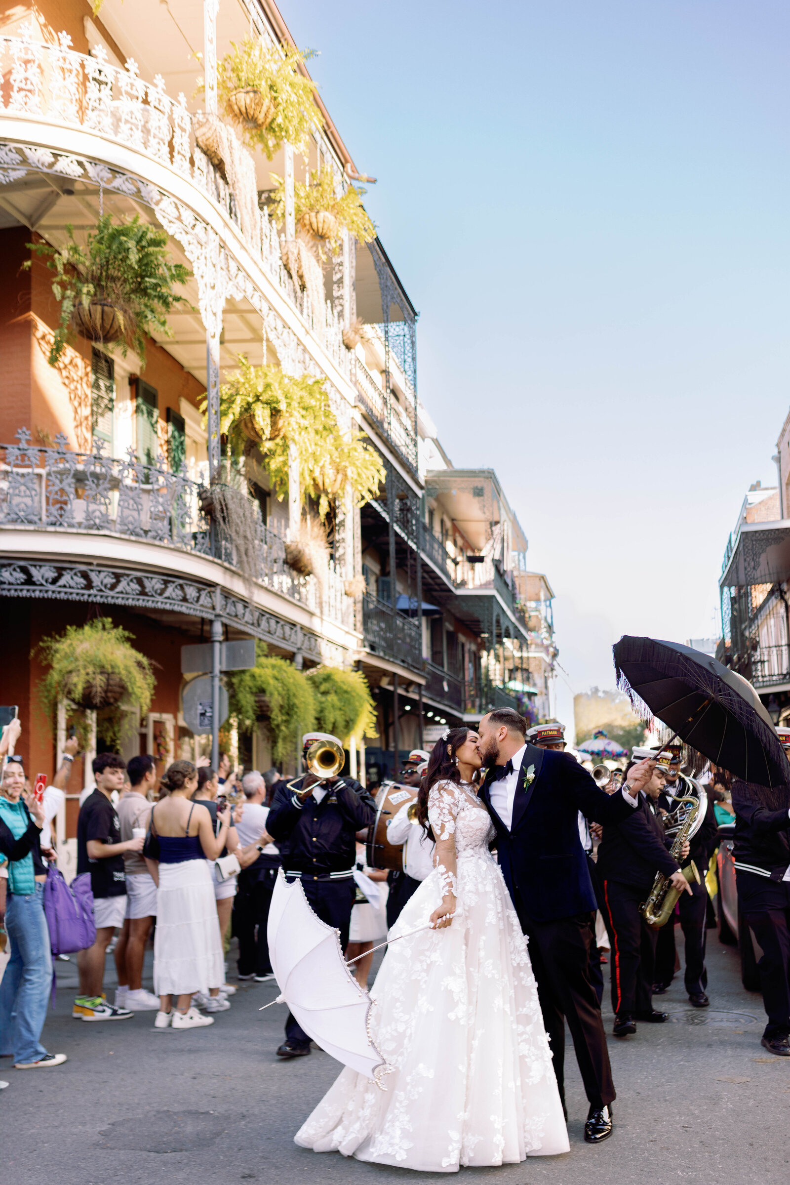 Couple kiss in a street of iron-lace balconies as a brass band and onlookers crowd around them.